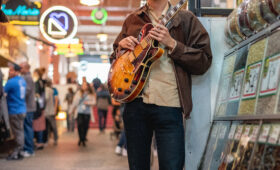 Student guitarist poses with instrument at an outdoor market in Los Angeles.
