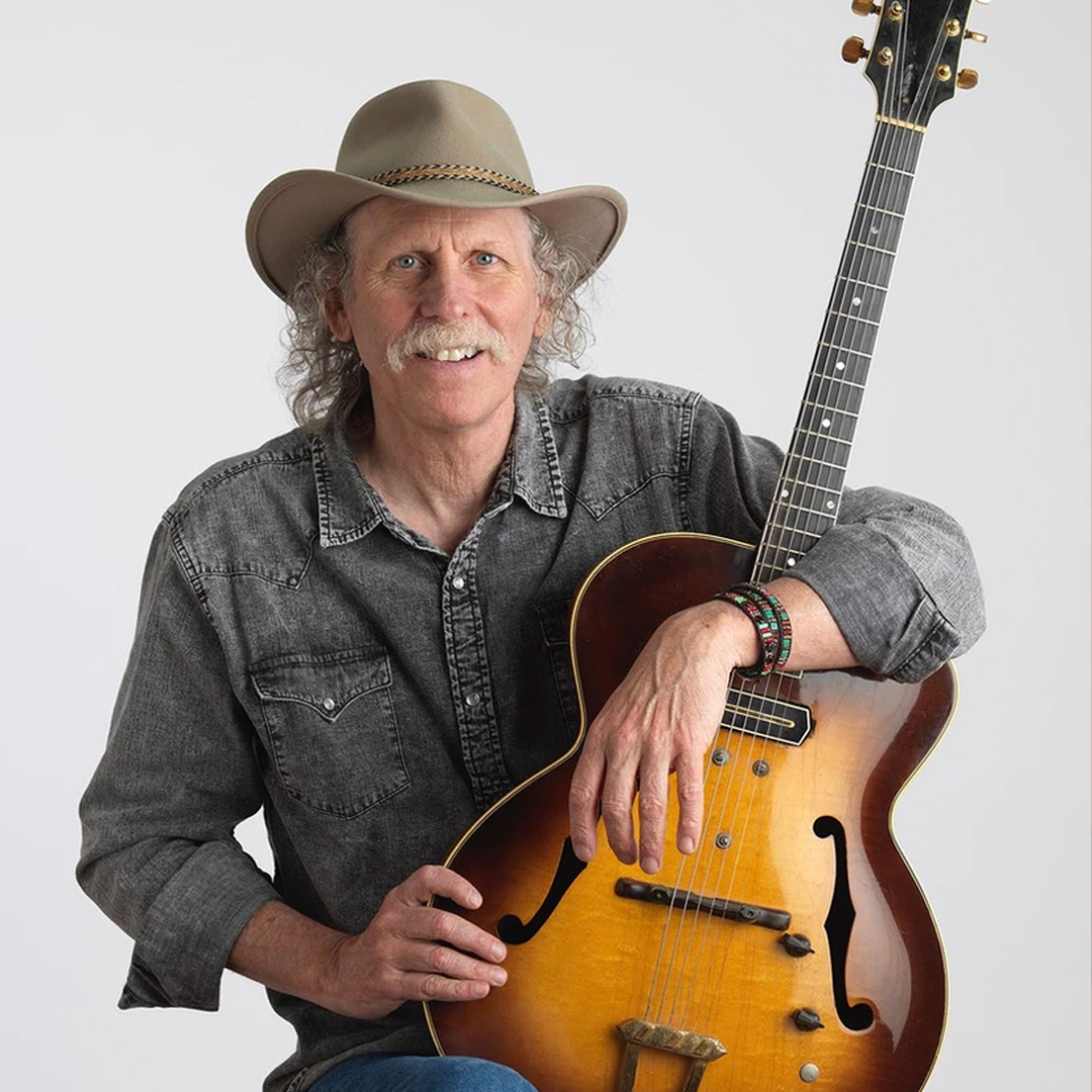 Bruce Forman holding a guitar and wearing a hat.
