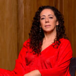 Luciana Souza wearing a red blouse and looking towards the camera while sitting.
