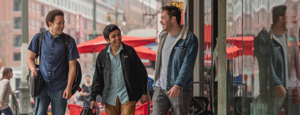 Smiling and laughing college-aged students walk together in a downtown environment.