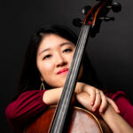 Stella Cho smiling towards the camera while holding a cello.