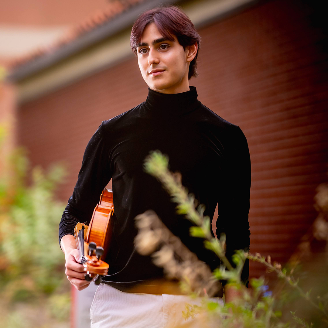 A photo of a college aged student holding a violin.