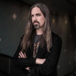 Photo of composer Bear McCreary looking toward the camera in front of a dark background.