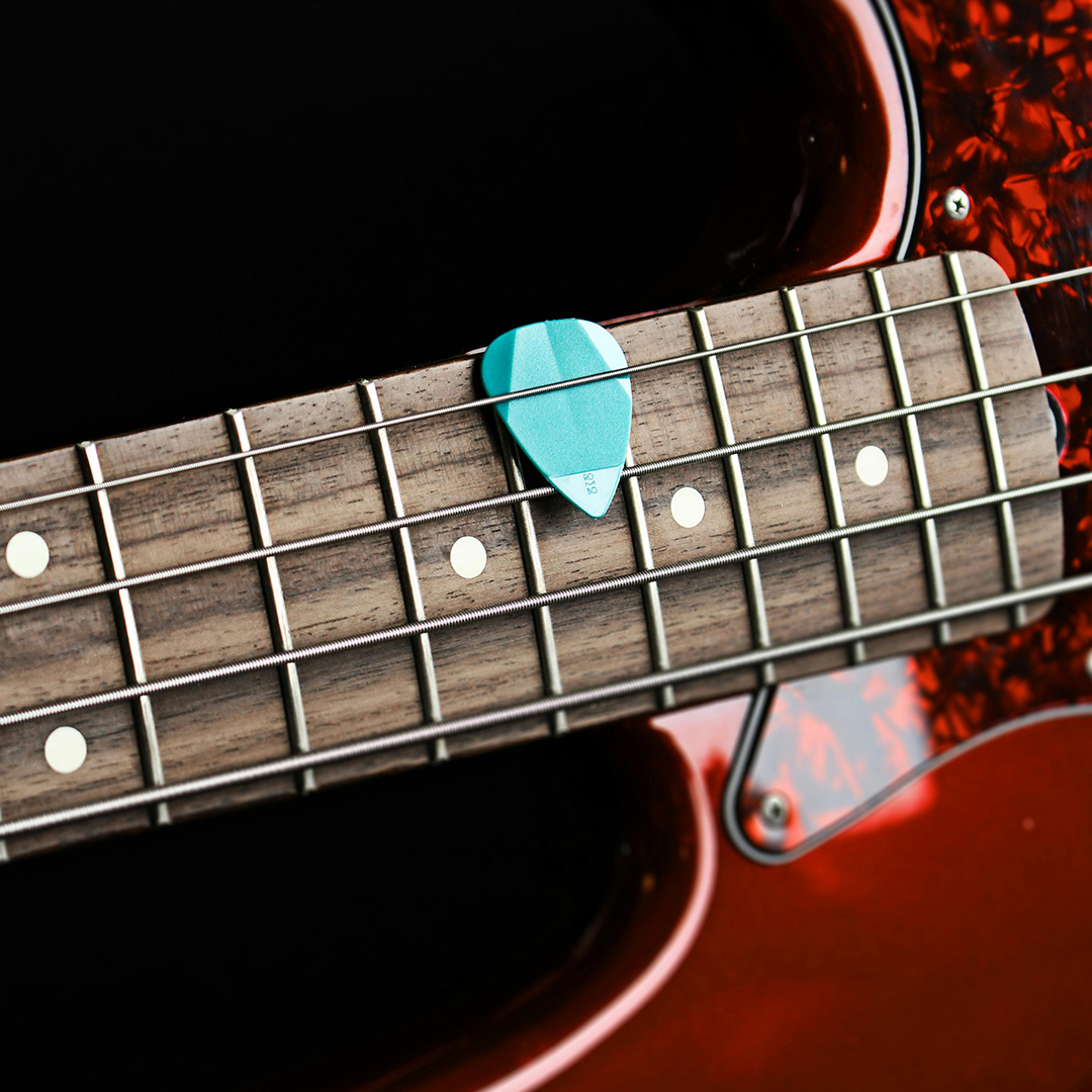 Up close photo of a guitar pick stuck between the strings of a red electric bass.