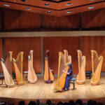 Kaitlin Miller performs on a concert stage playing the harp.