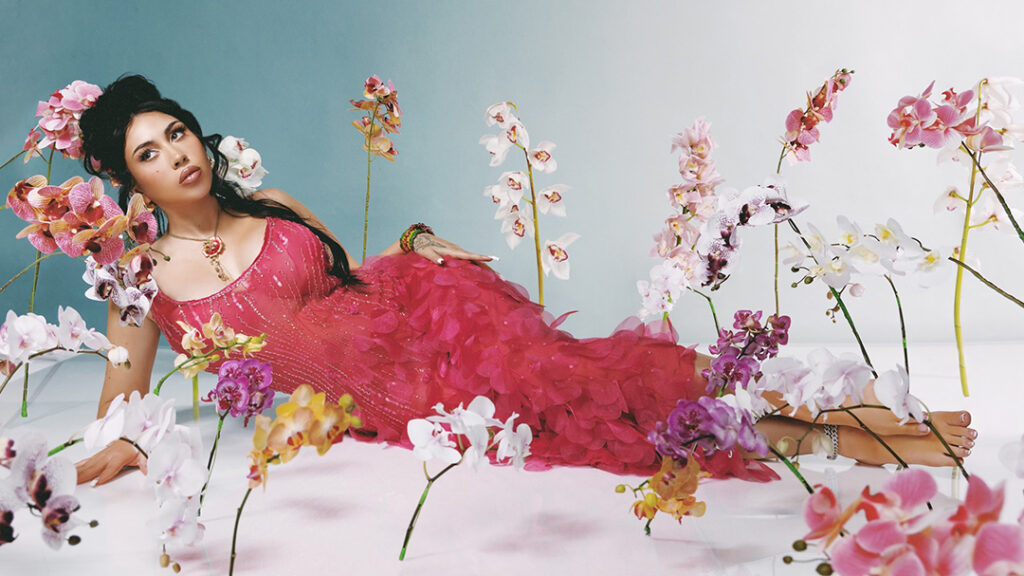 Photo of performer Kali Uchis wearing a red dress surrounded by flowers.
