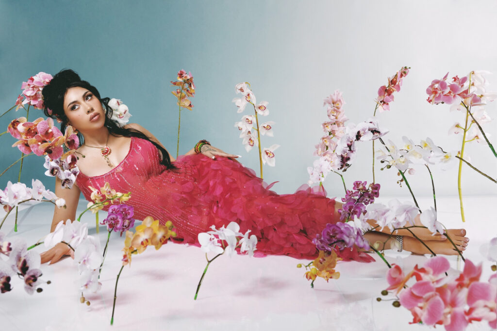 Photo of performer Kali Uchis wearing a red dress surrounded by flowers.