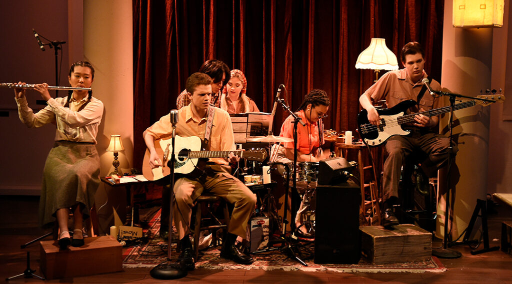 Photo of a jazz band featuring composer Oliviana Marie playing on stage during the production of an indoor play.