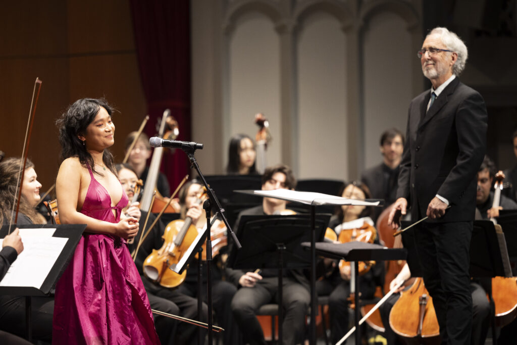 Photo of a smiling performer on stage with a symphony orchestra.