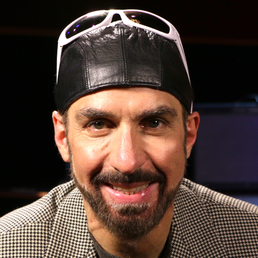 Bobby Borg wearing a black leather cap with white sunglasses and smiling at the camera.