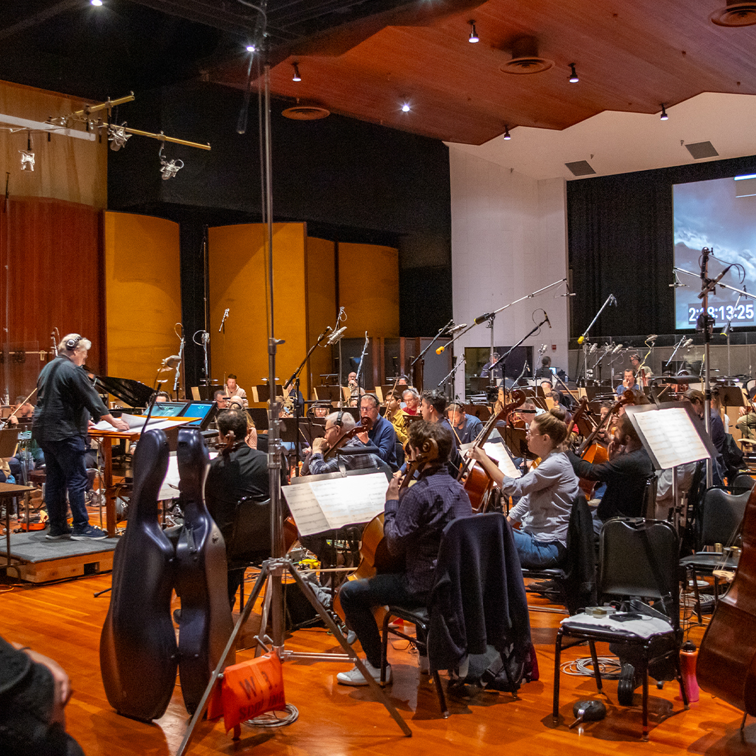 An orchestra gathers in a large studio soundstage.