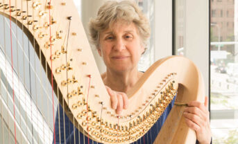 Harpist JoAnn Turovsky looking into the camera next to her instrument.