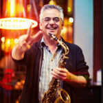 Photo of Sal Lozano holding a saxophone and smiling.