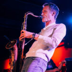 Photo of saxophonist Bob Reynolds performing on stage at an indoor music venue.