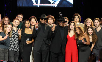 A group of college-aged students gather on stage after a performance.