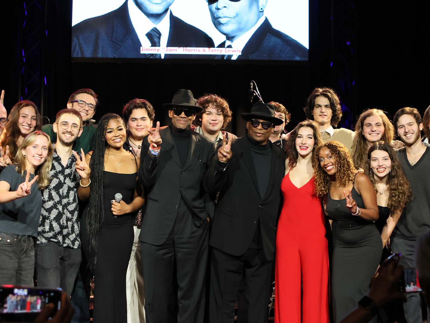 A group of college-aged students gather on stage after a performance. 