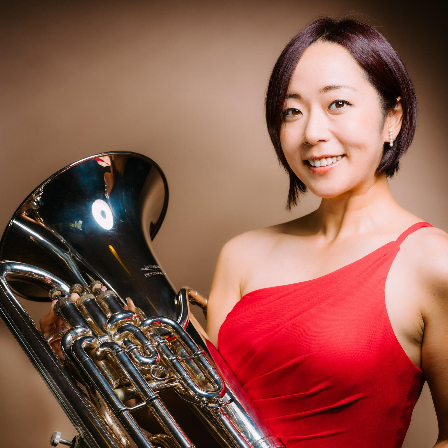 A woman in a red top smiles and holds a euphonium