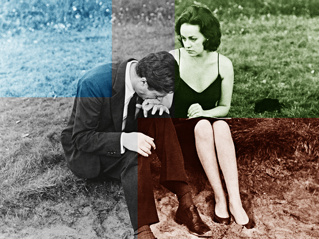 A man and woman sit on a sandy dune in formal attire.