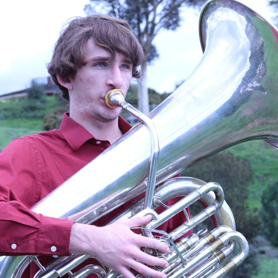 A man in a red shirt plays a tuba outdoors