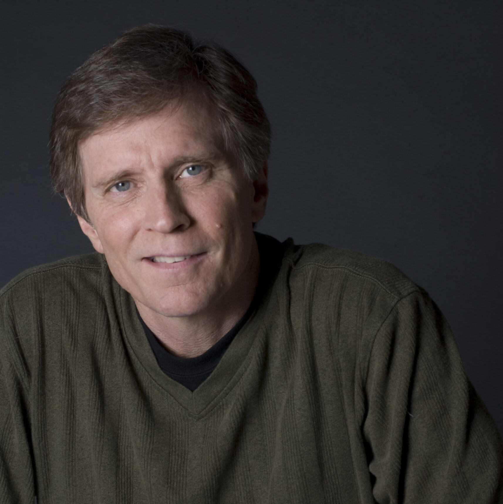 A man in a dark green sweater sits and poses for the camera