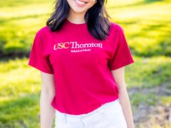 A smiling college student outdoors wearing a red shirt.