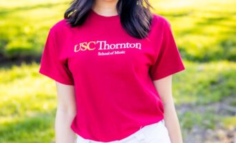 A smiling college student outdoors wearing a red shirt.