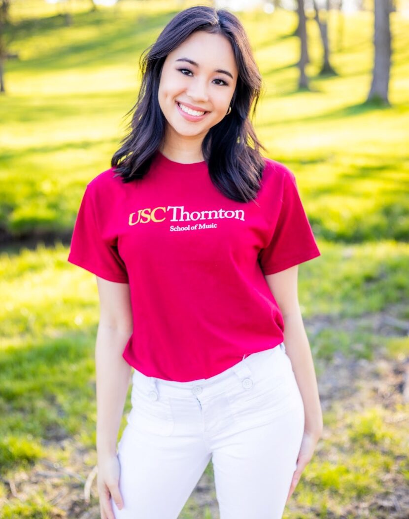 A smiling college student outdoors wearing a red shirt.