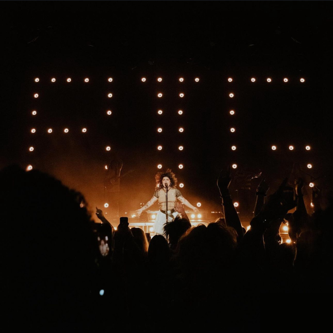 Photograph of a woman on stage with a crown in the foreground.