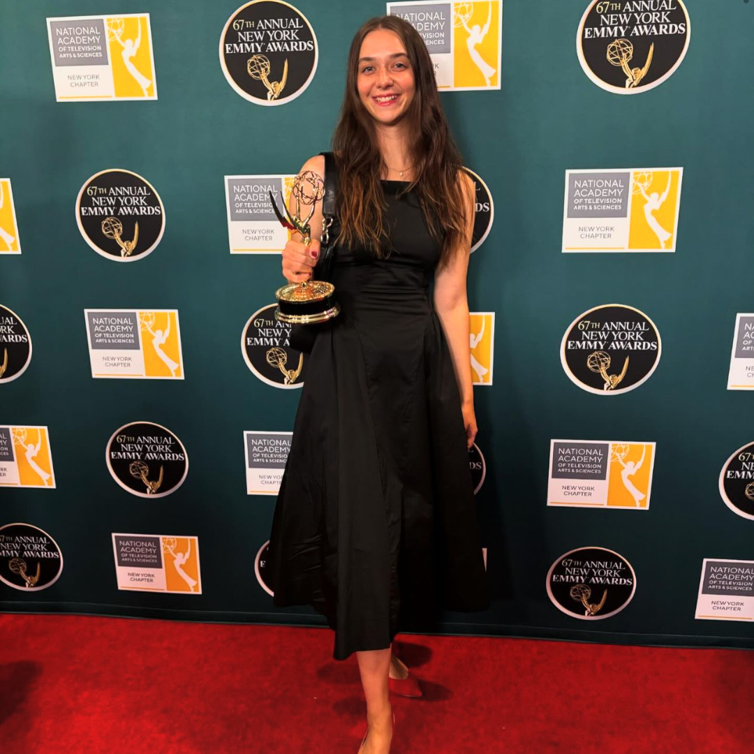 Photo of a woman in a black dress on a red carpet holding an Emmy award.