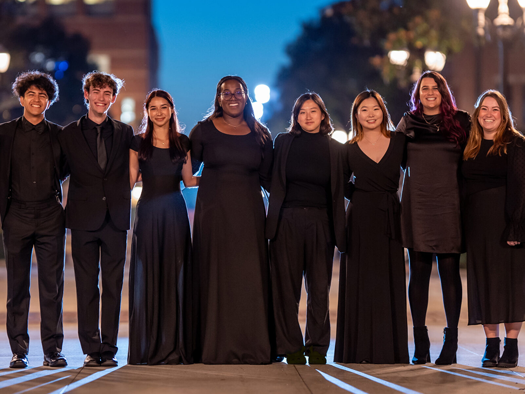 Choral students smile for the camera at blue hour on the USC campus.