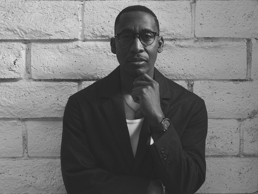 Black and white photo of producer Raphael Saadiq leaning against a wall