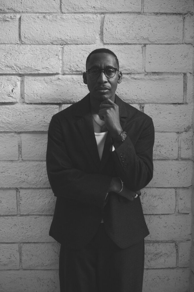 Black and white photo of producer Raphael Saadiq leaning against a wall