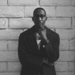 Black and white photo of producer Raphael Saadiq leaning against a wall