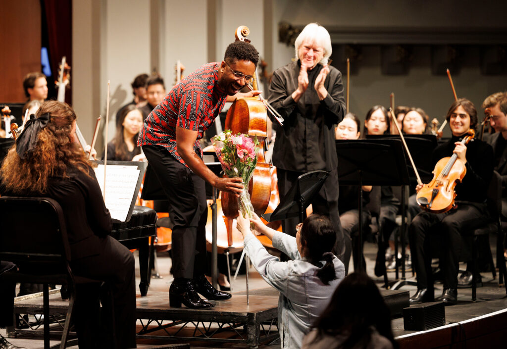 A cellist accepts a bouquet of flowers on stage.