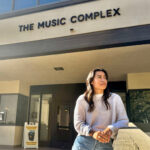 A woman stands in front of a building named "The Music Complex."