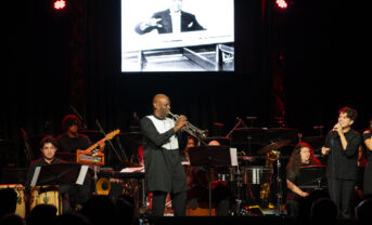 A trumpeter plays center stage surrounded by an ensemble.