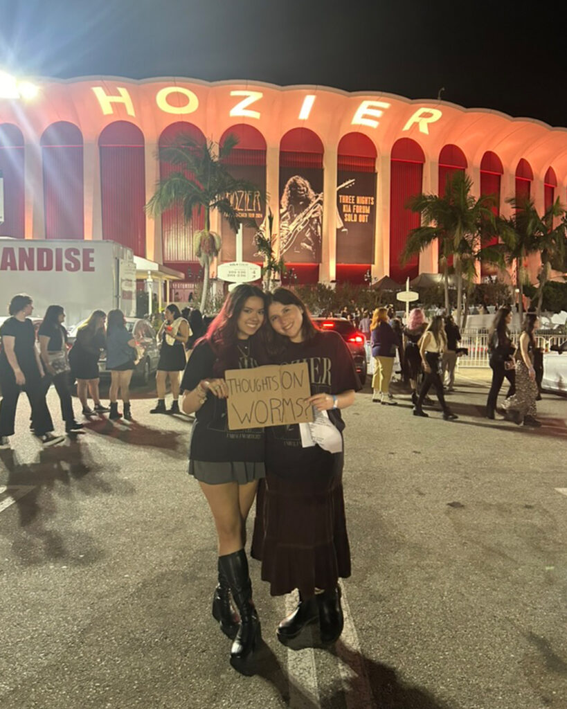 Hannah Wolf with a friend post-concert at the Forum, holding a sign that says "Thoughts on Worms?"