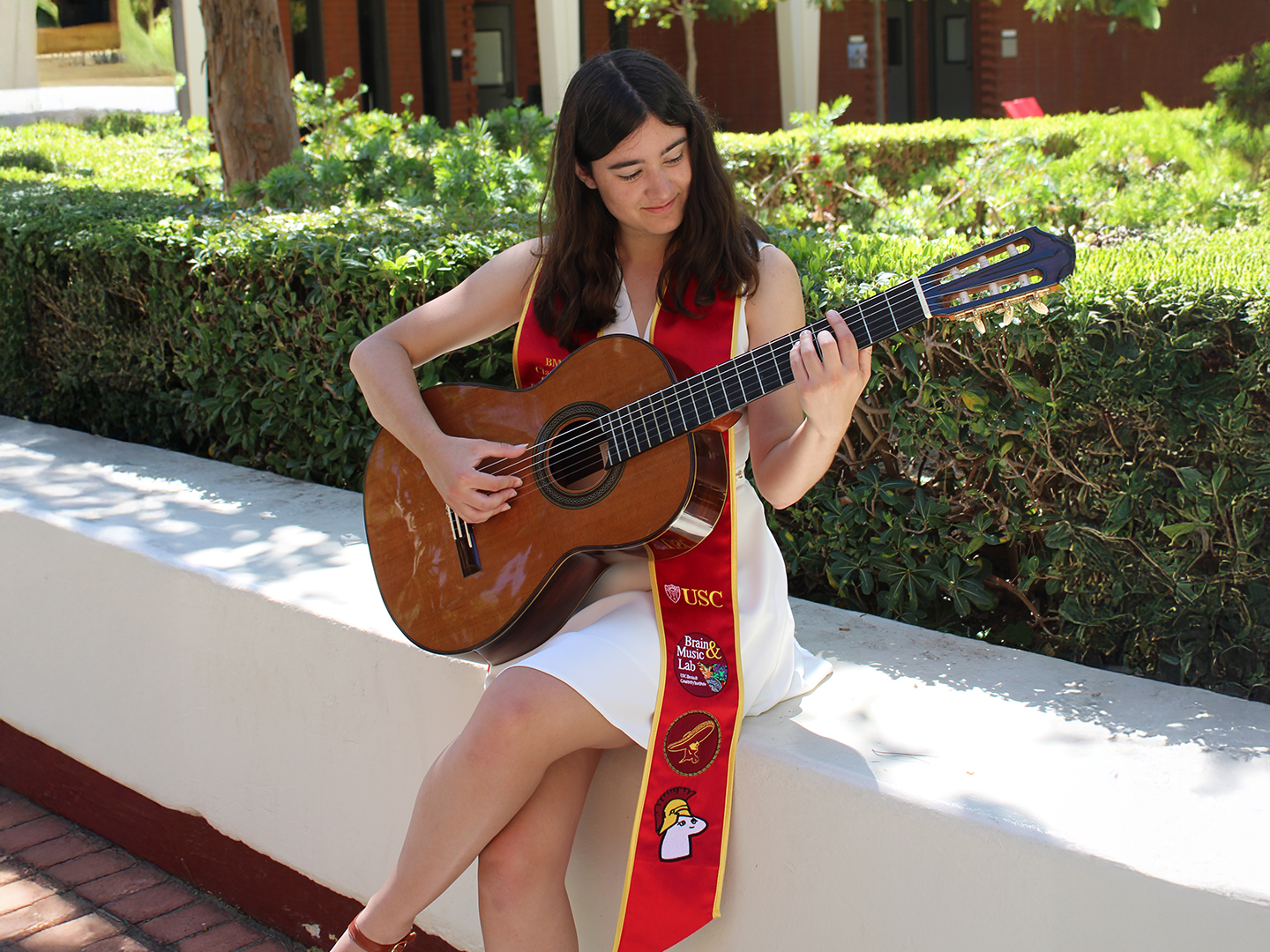Ashley Melendres plays the guitar, wearing a white dress and decorated Commencement sash.