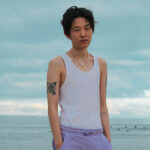 A musician stands in front of the ocean.