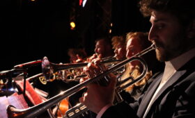 A brass section plays onstage