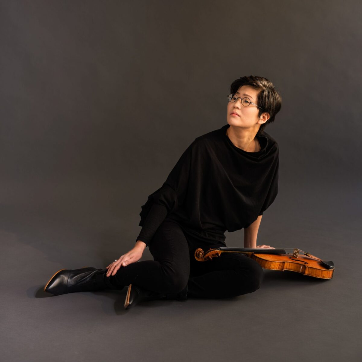 A violinist sits on the ground with their violin across their lap.