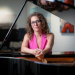 artist seated at a piano, starting at the camera