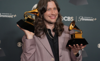 Man smiles while holding two Grammy awards.