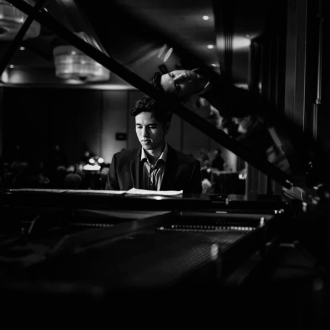 Black-and-white close up photo of man sitting in front of piano.