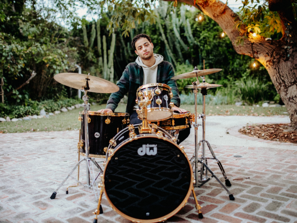 Young musician poses behind a set of drums.