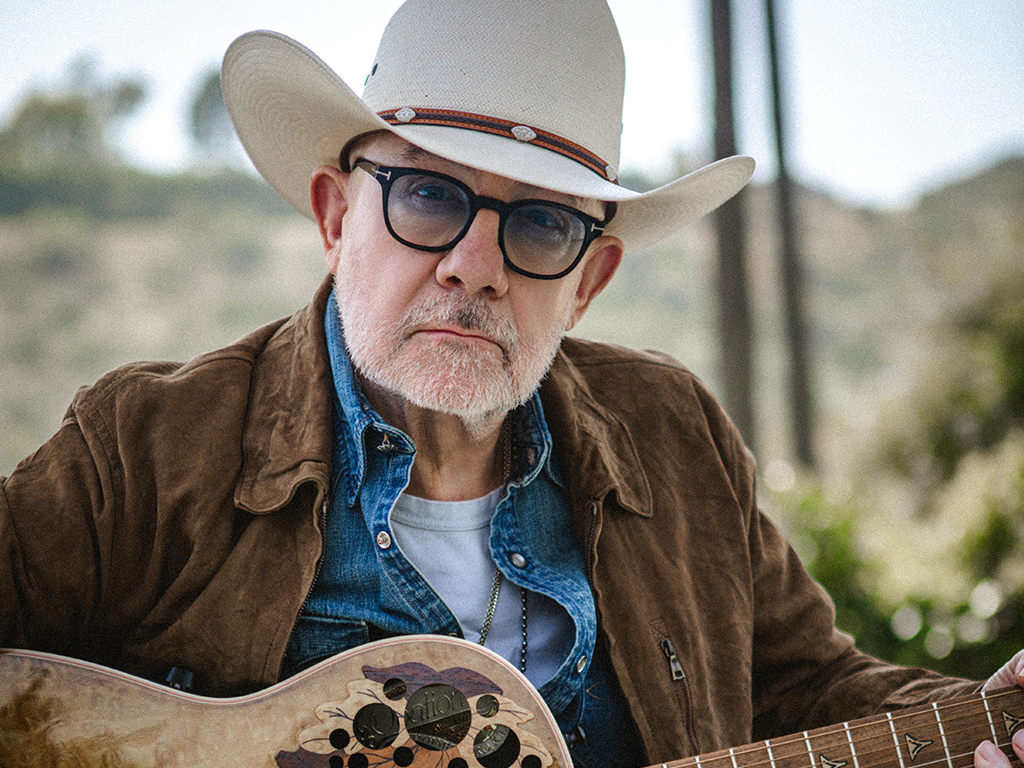Bernie Tapuin holds a guitar with a desert background.