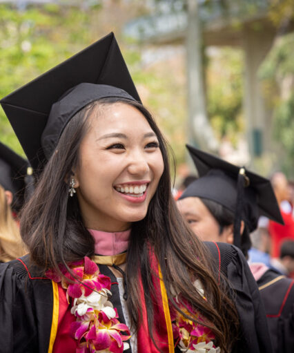 Smiling college students dressed in graduation gowns & regalia.