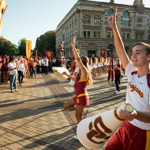 USC students in cheerleading and spirit attire engaging with a crowd.