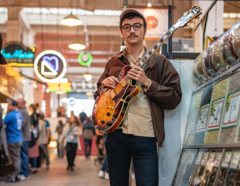 Student guitarist poses with instrument at an outdoor market in Los Angeles.