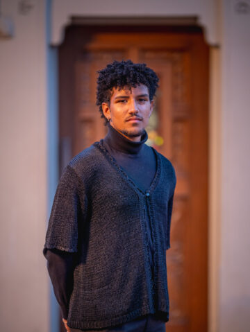 Choral student in layers of concret black attire poses in front of an ornate doorway.